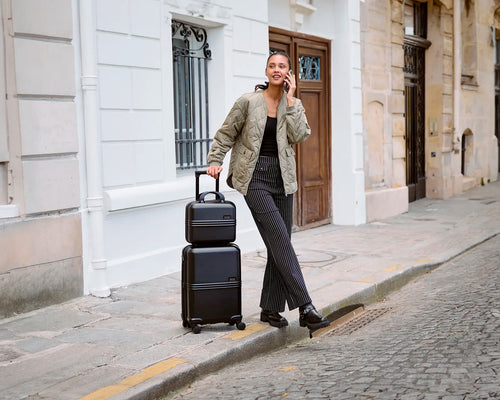 Woman holding a black ELLE Expedition luggage set in the streets of Paris